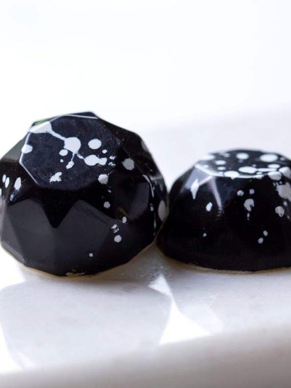 side view two black in white speck chocolate candy on a white stand